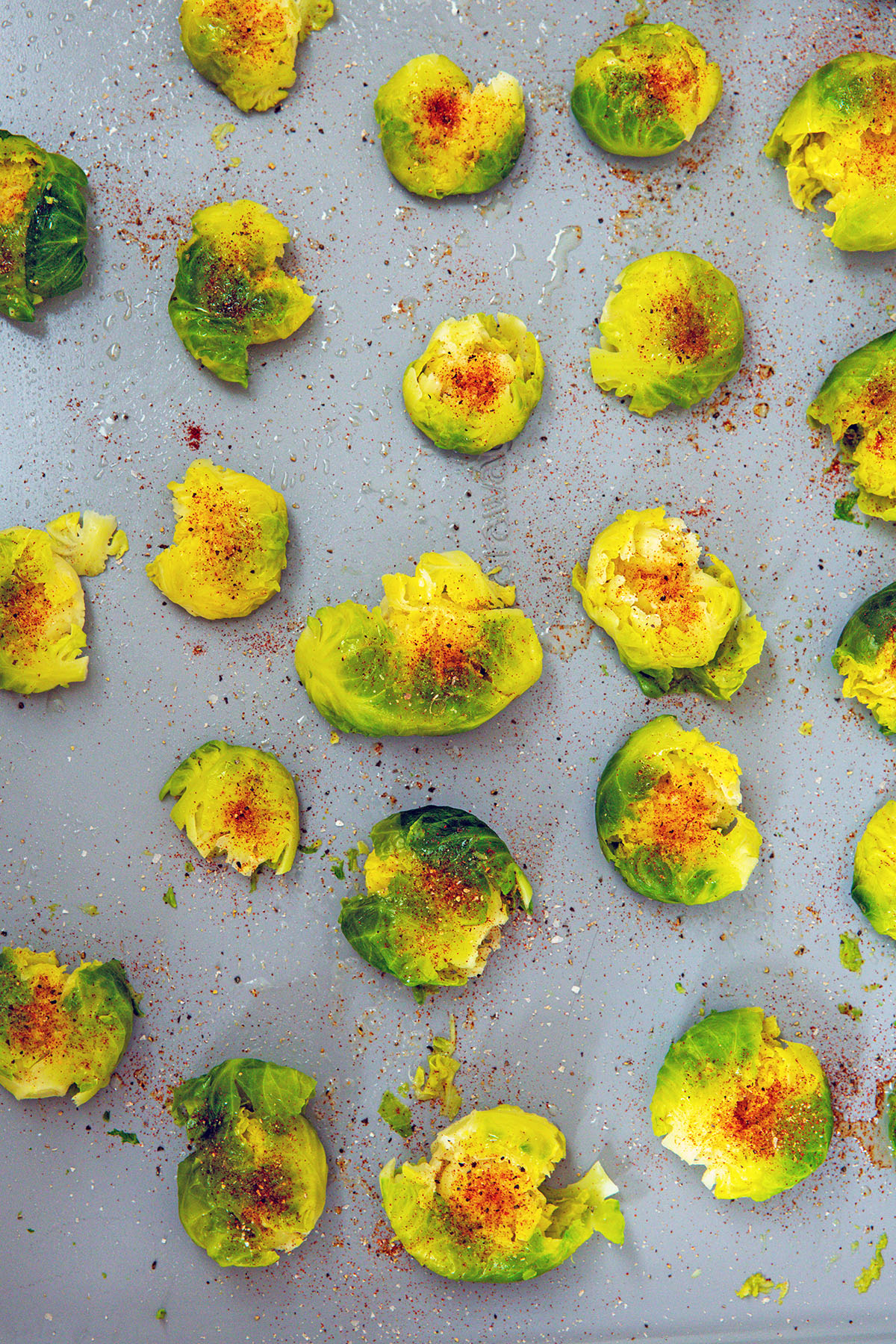 Blanched brussels sprouts blanched on baking sheet with spices on them.