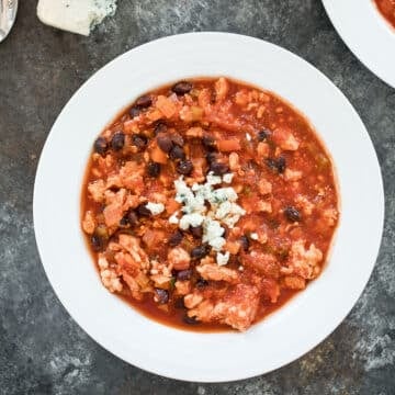 Closeup overhead view of a bowl of buffalo chicken chili topped with crumbled blue cheese.