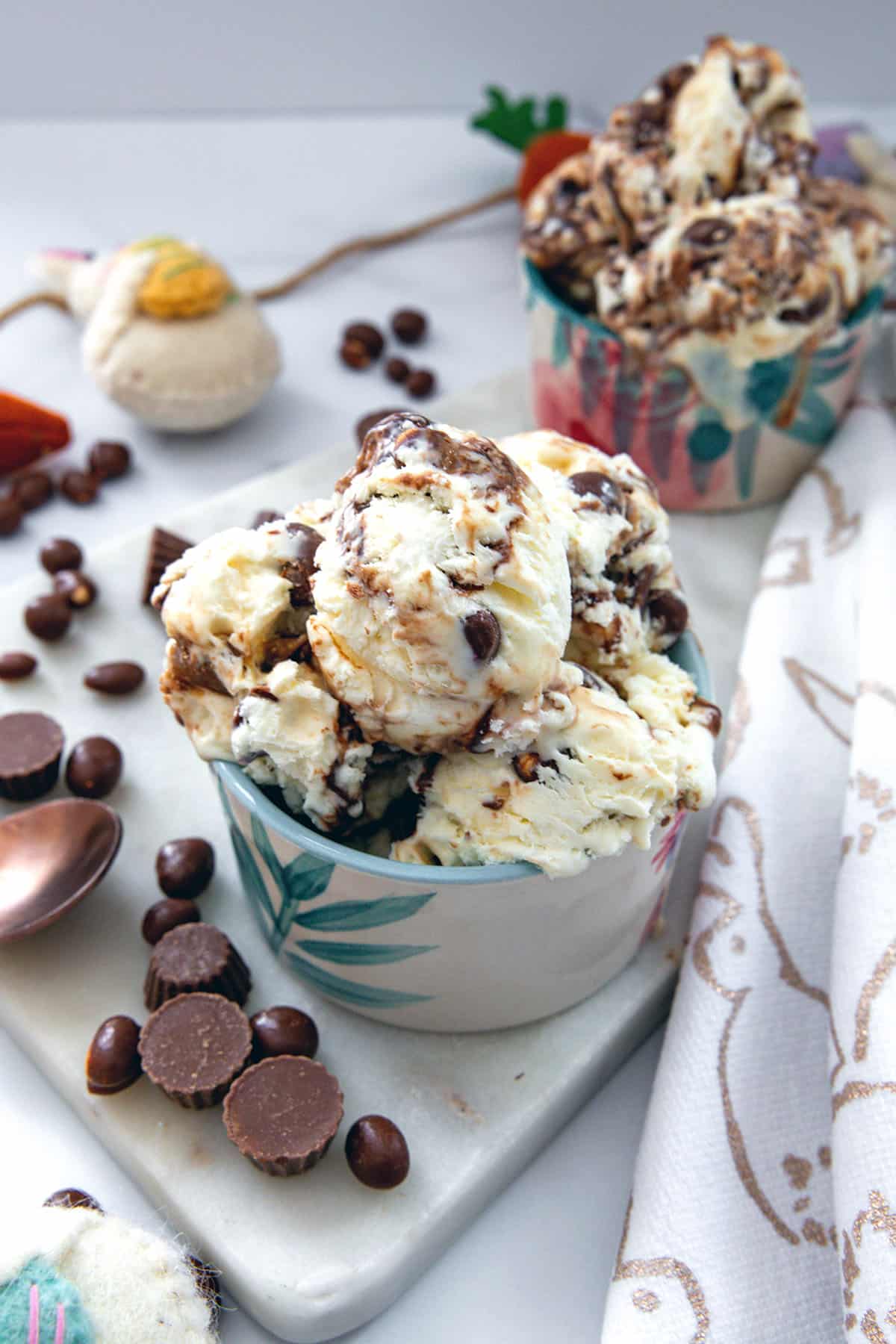 Two bowls of ice cream with mini peanut butter cups and chocolate peanuts all around.