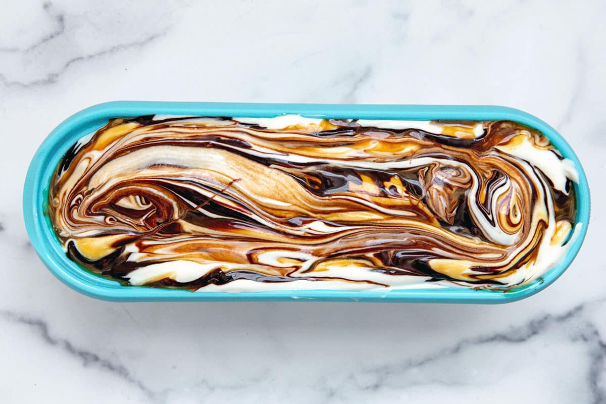Ice cream with chocolate sauce and caramel sauce swirl in large ice cream container.