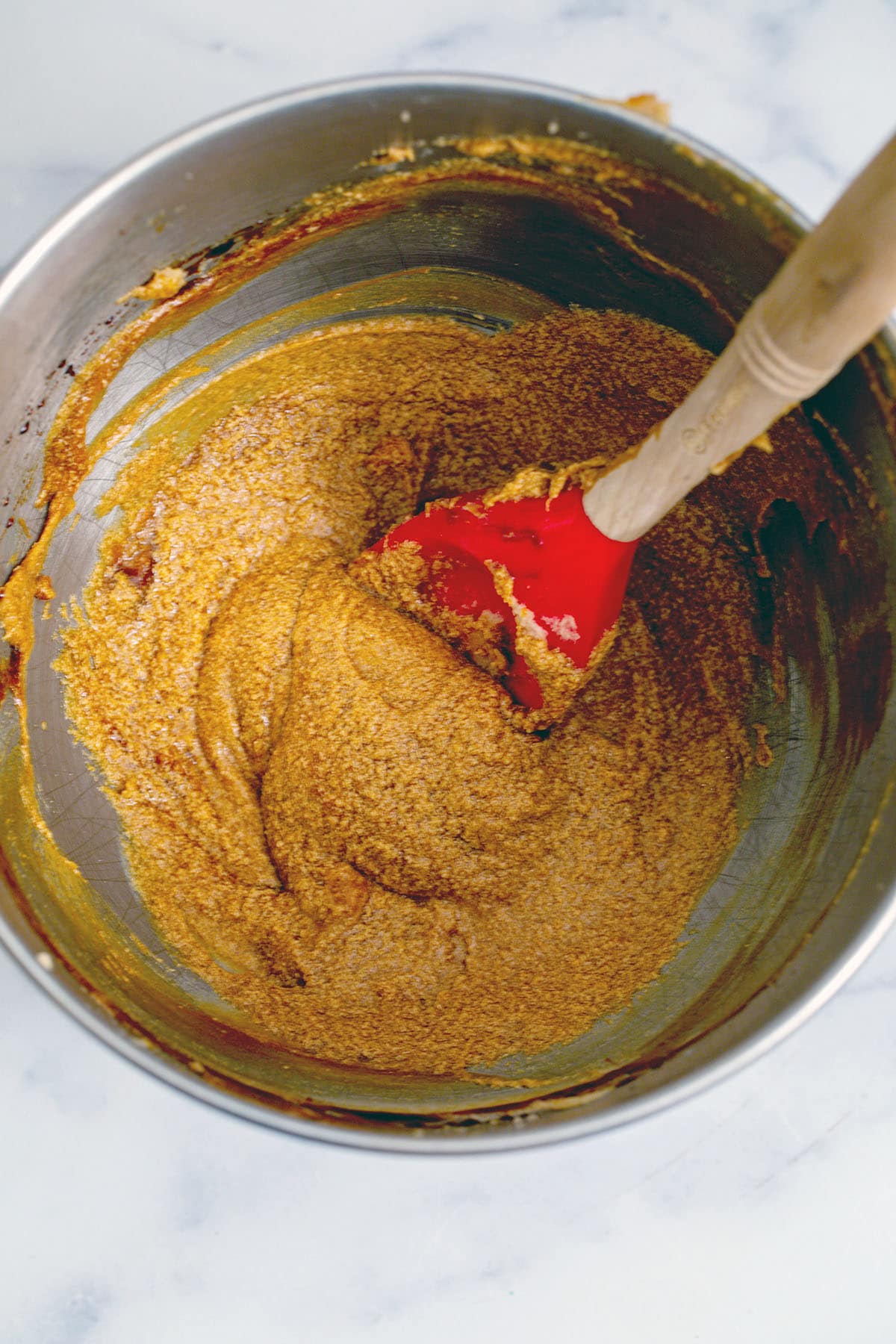 Butter and brown sugar creamed together with eggs and molasses in mixing bowl with spatula.