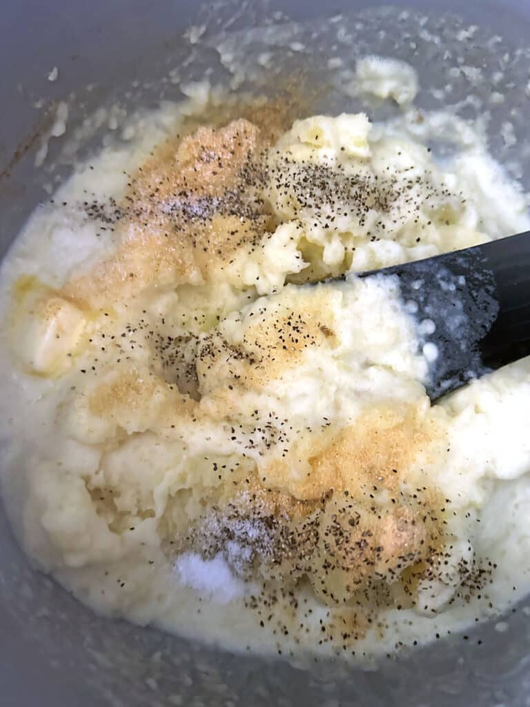 Milk and cream mixture, garlic powder, pepper, and minced garlic in mashed potatoes in pot.