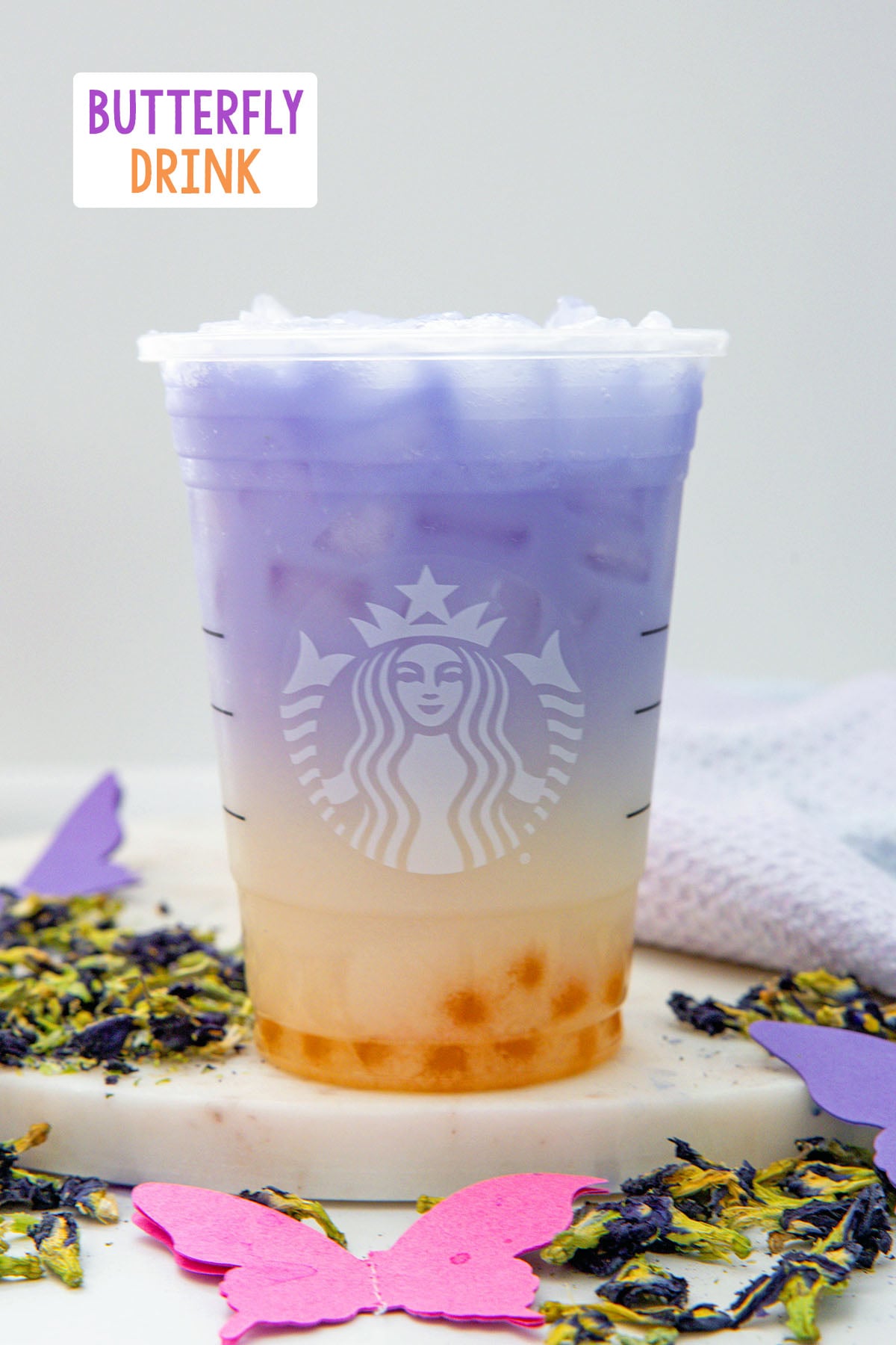 Head-on view of a Butterfly Drink in a Starbucks cup with butterfly pea flowers all around and recipe title at top.