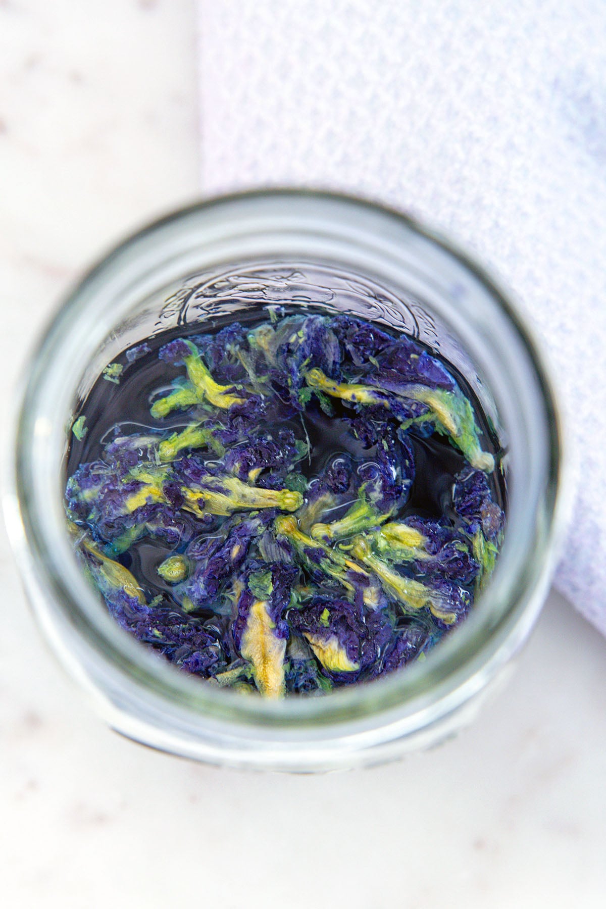 Overhead view of dried butterfly pea flowers in water in mason jar.