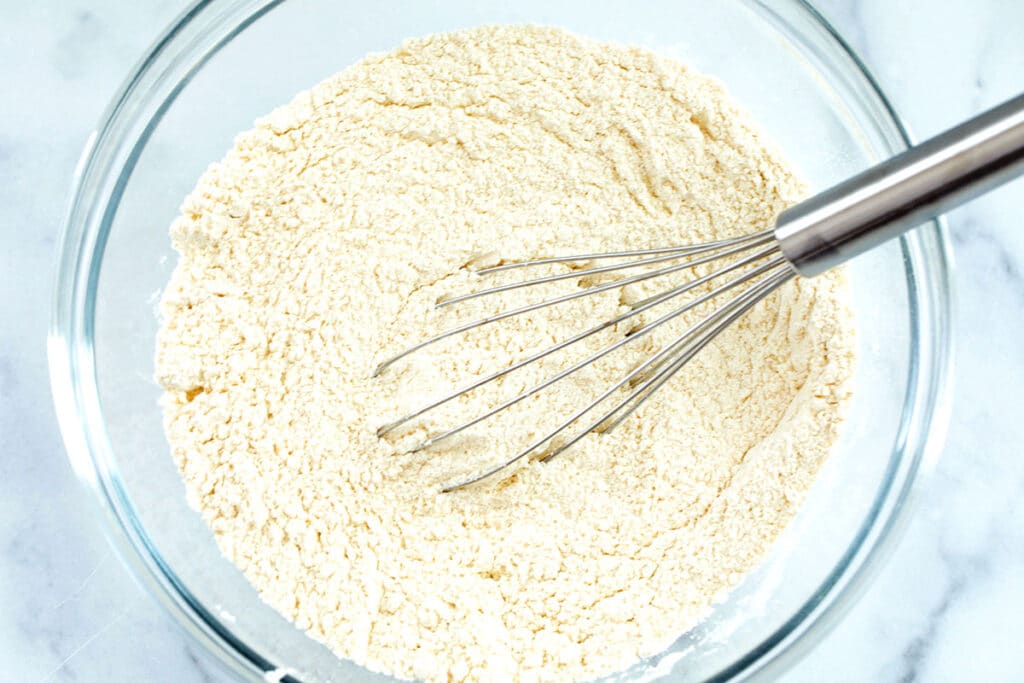 Flour, sugar, and other dry ingredients in bowl with whisk.