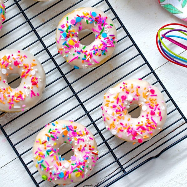 Overhead view of baked buttermilk donuts with colorful sprinkles on a black baking rack.