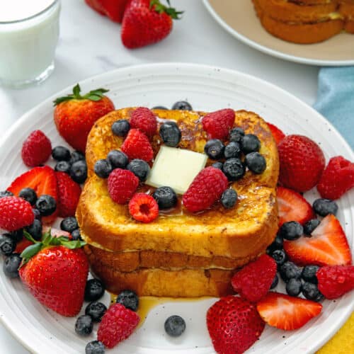 Closeup view of a stack of buttermilk french toast with pat of butter and berries.