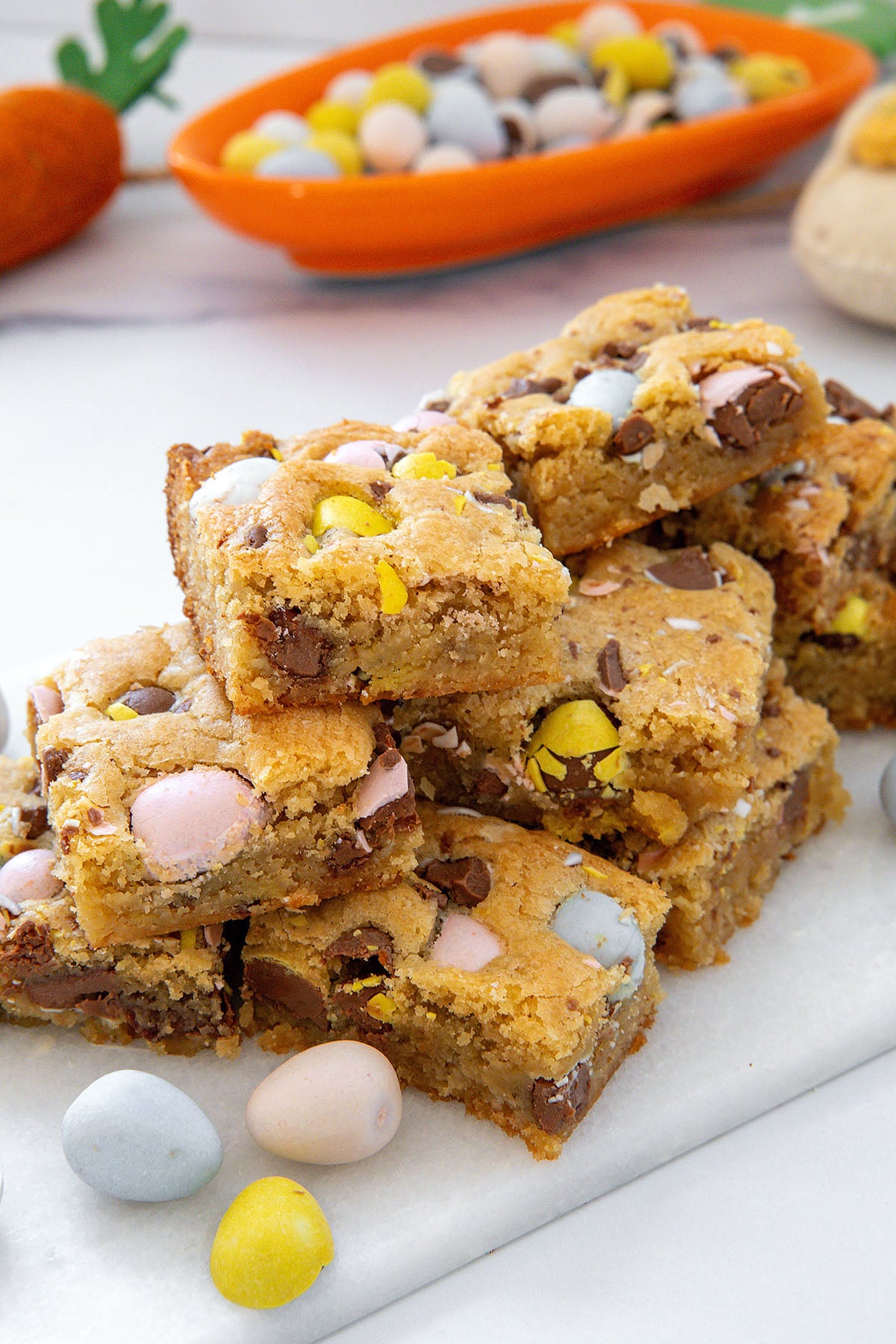 Cadbury Mini Egg blondies in a stack on a marble platter with candies all around.