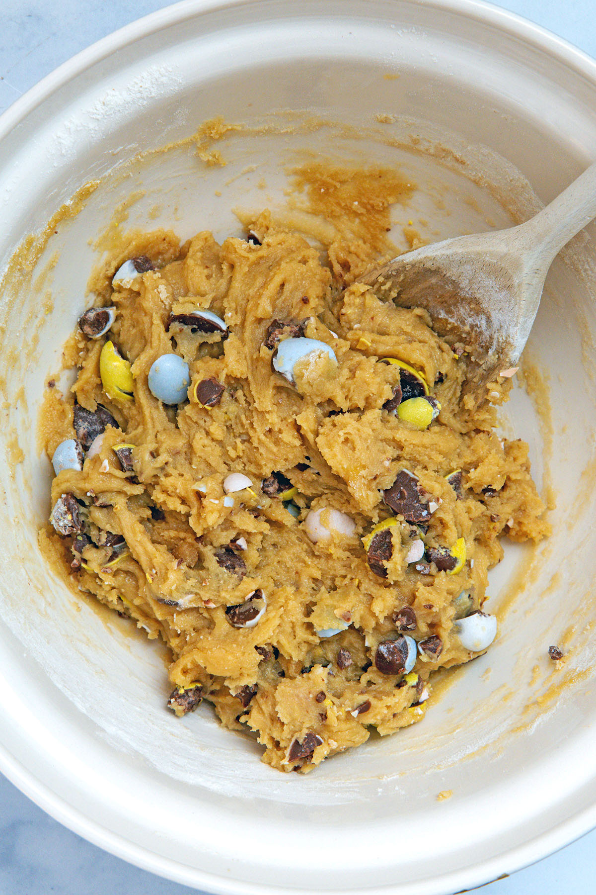 Chopped Cadbury Mini Eggs in blondie batter with wooden spoon.