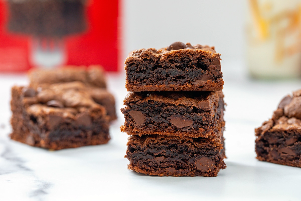 Landscape head-on view of stack of brownies with more brownies and box of cake mix in background.