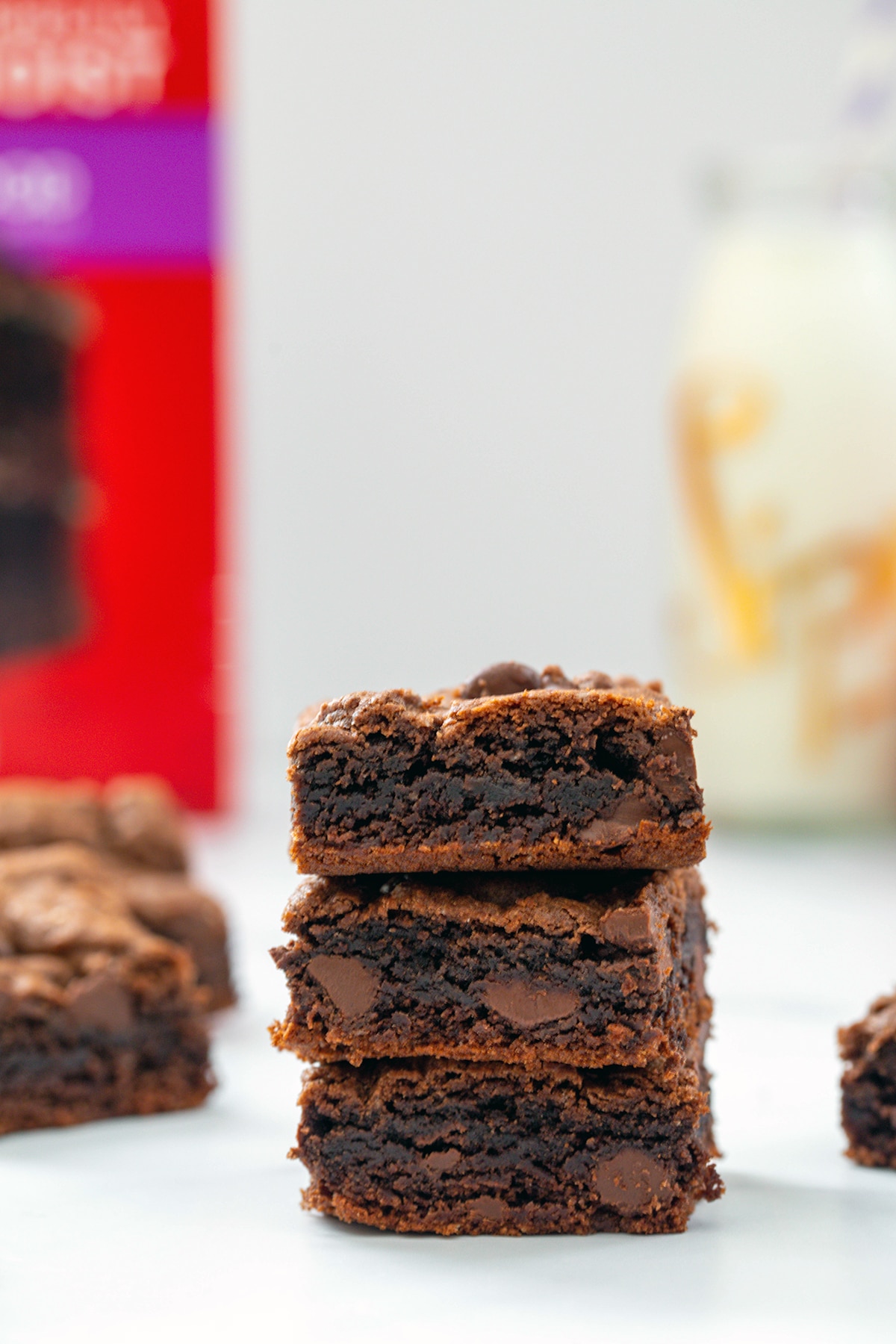 Head-on stack of cake mix brownies with cake mix box and glass of milk in background.