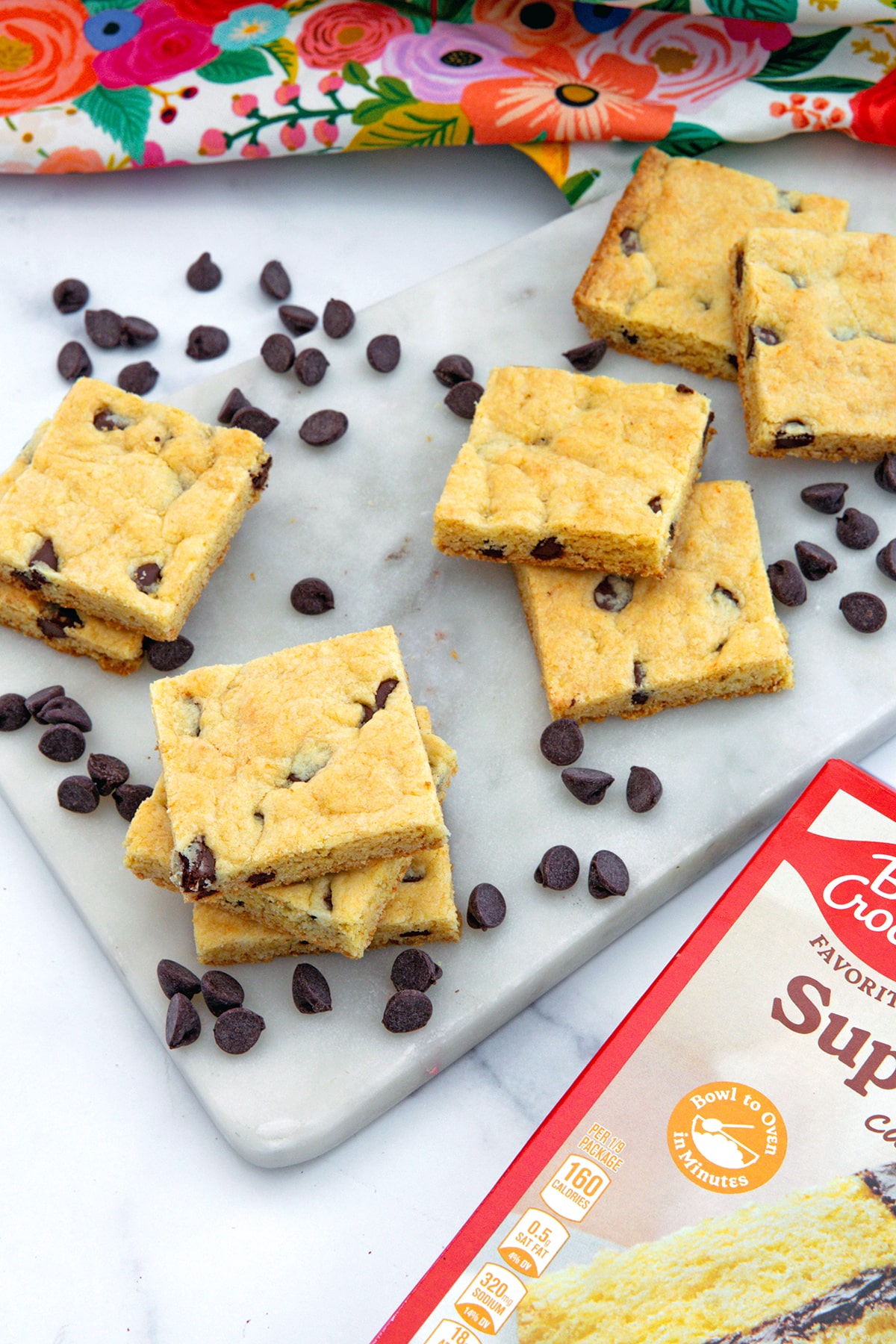 Overhead view of chocolate chip cake mix cookie bars with chocolate chips all around and box of yellow cake mix in foreground.