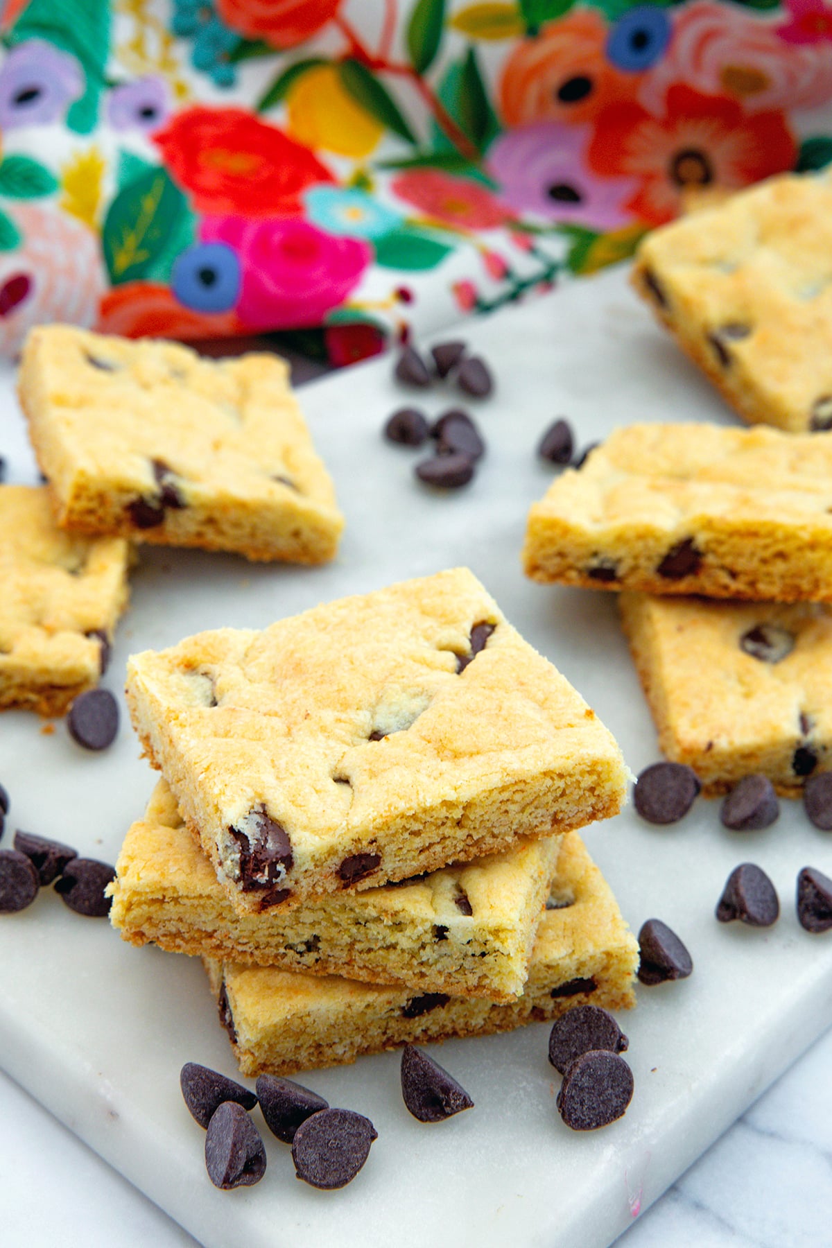 Stack of cake mix cookie bars with more in background, along with chocolate chips all around.