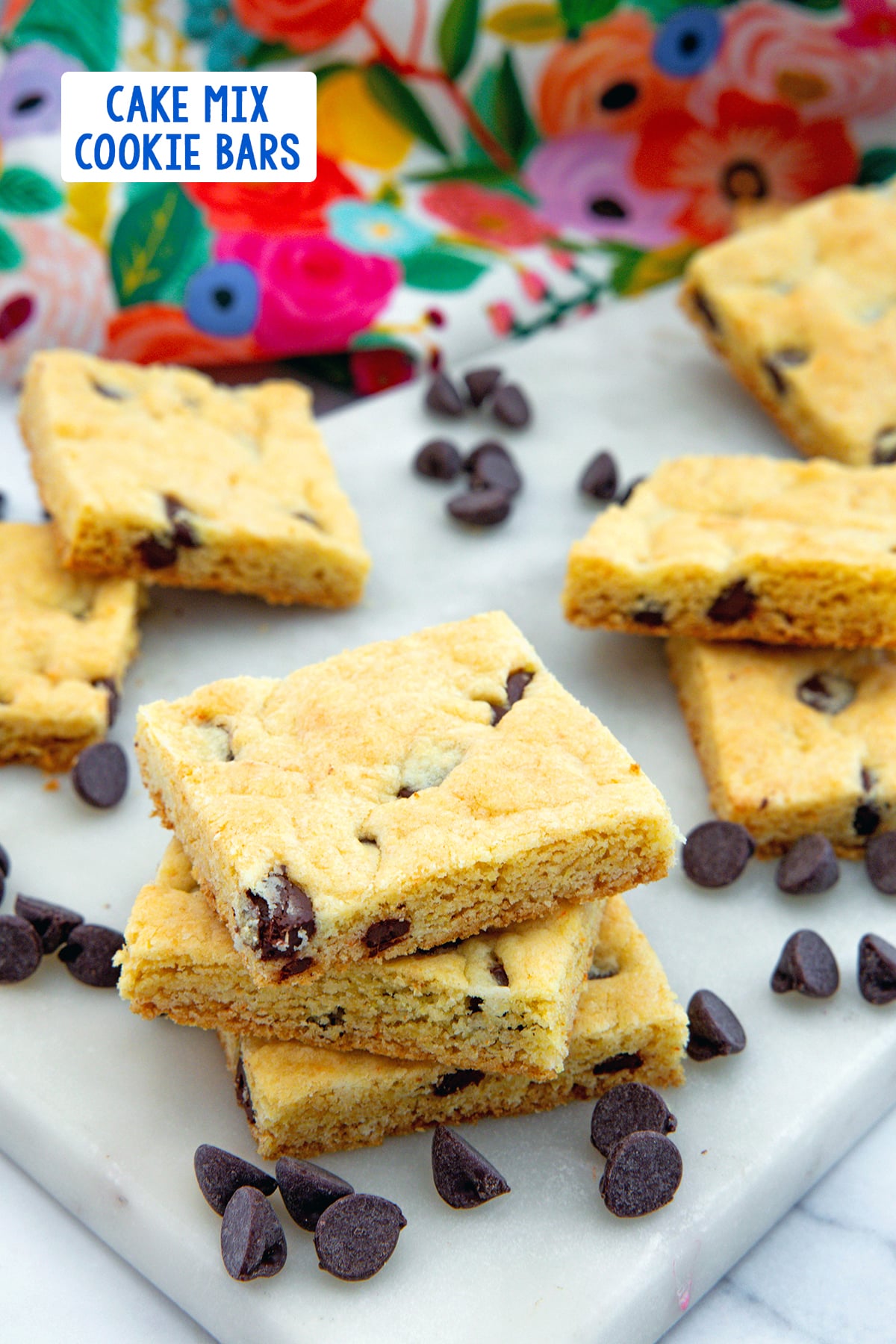 Stack of cake mix cookie bars with more in background, along with chocolate chips and recipe title at top.