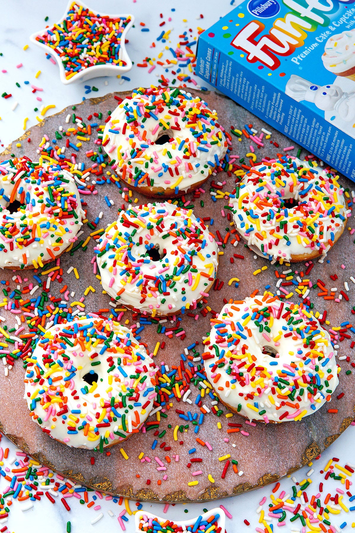 Overhead view of vanilla frosted cake mix donuts with rainbow sprinkles with box of Funfetti cake mix in background.