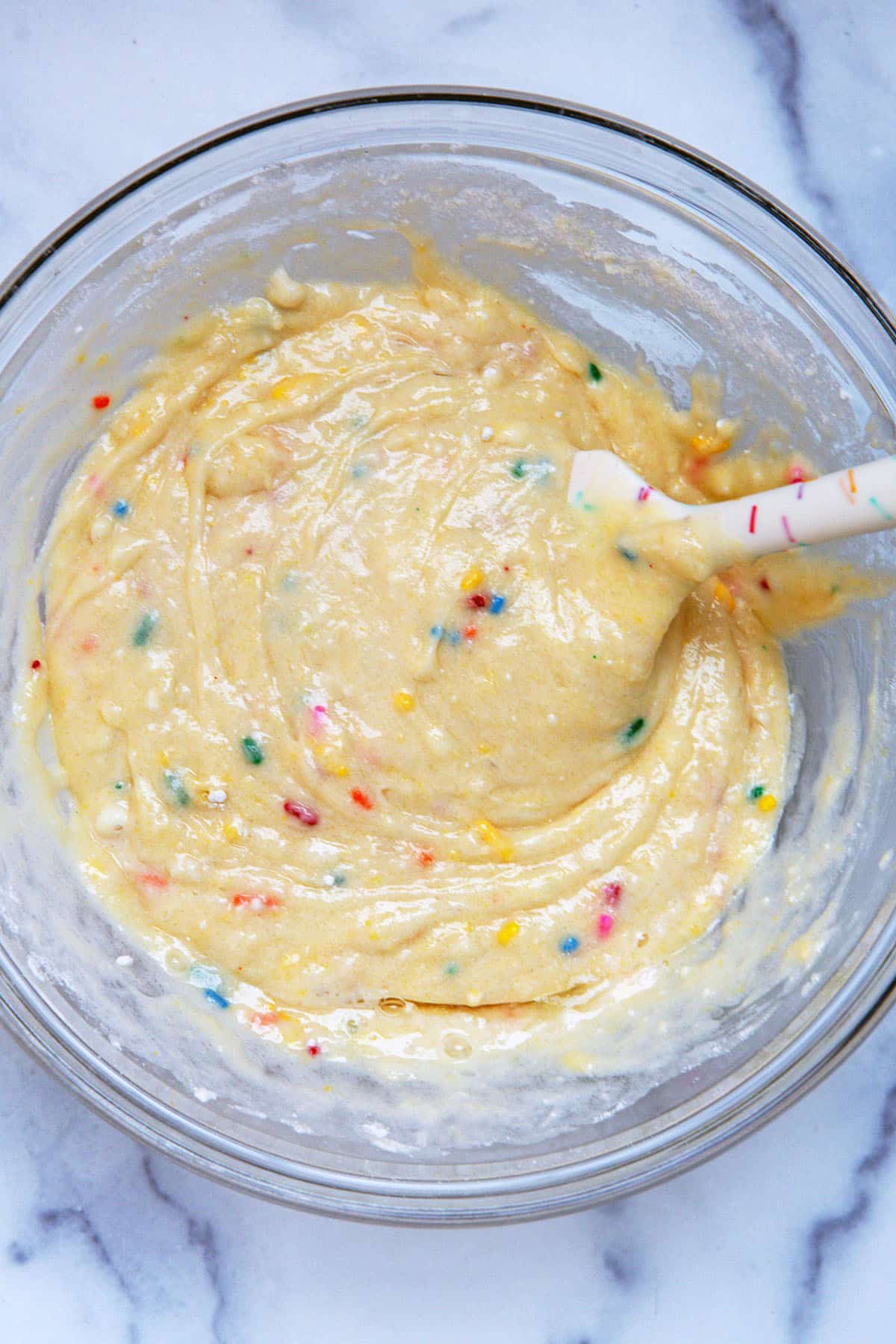 Funfetti cake mix donut batter in mixing bowl with spatula.