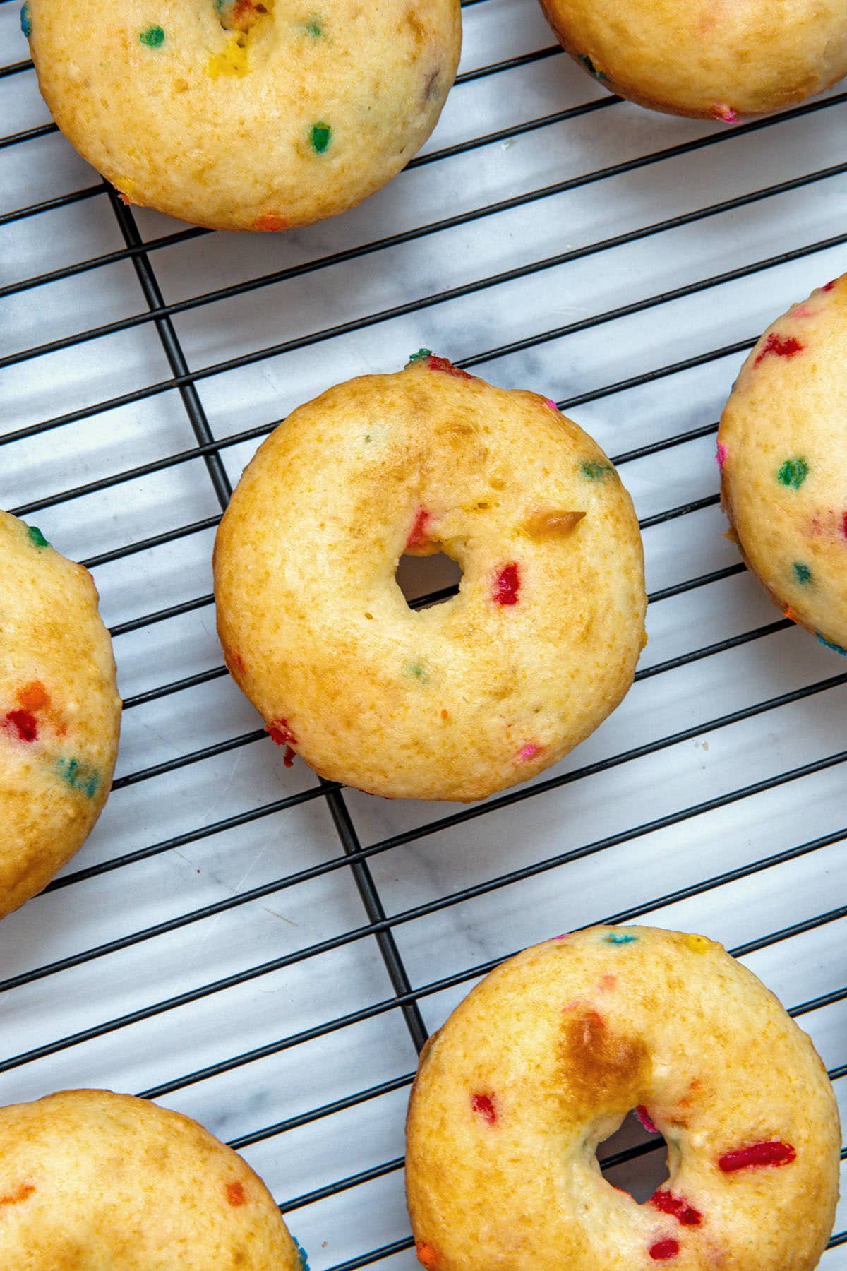 Funfetti cake mix donuts cooling on a metal rack.
