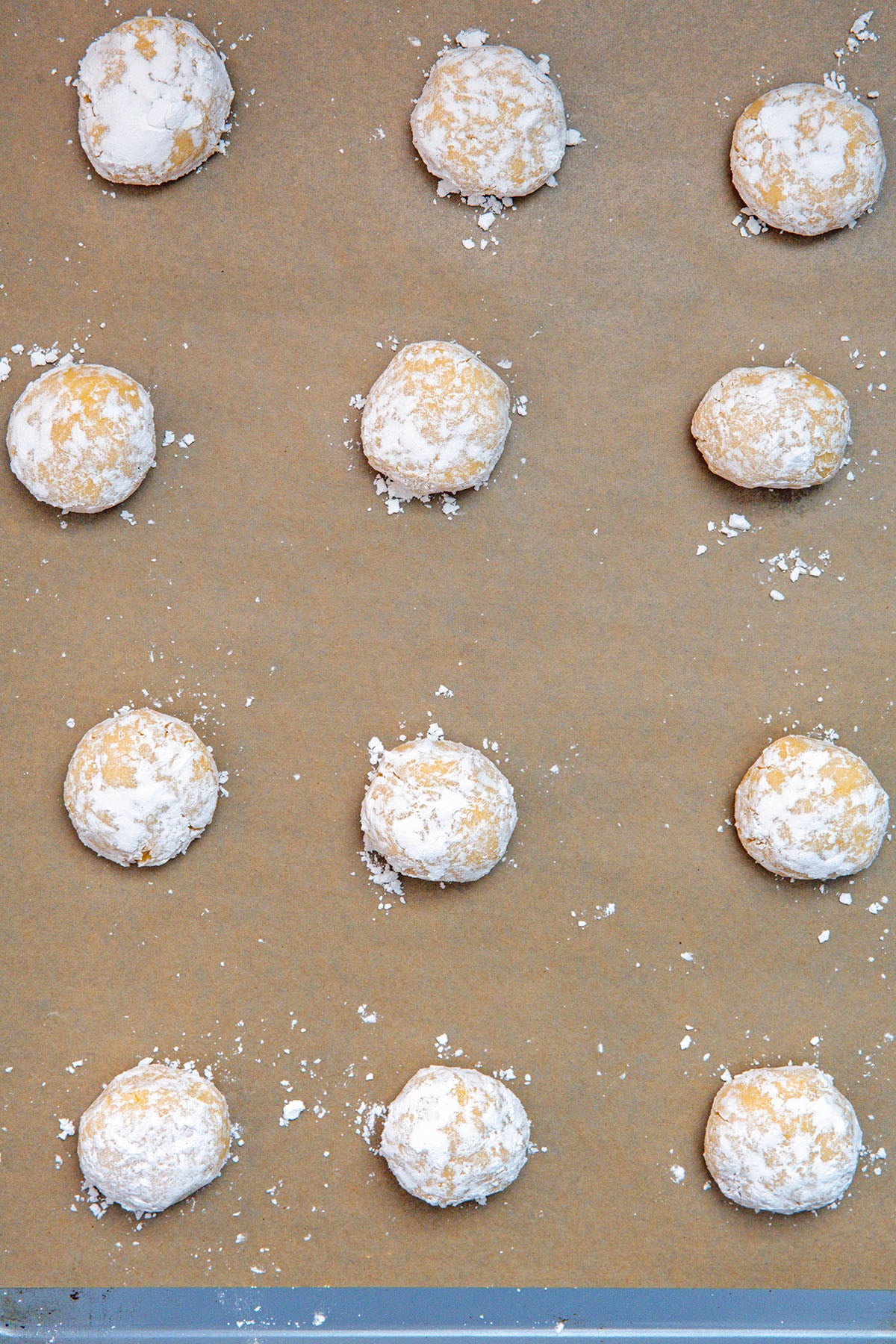Lemon cake mix cookie dough balls coated in powdered sugar on parchment paper-lined baking sheet.