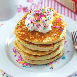 Stack of cake mix pancakes topped with frosting and sprinkles.