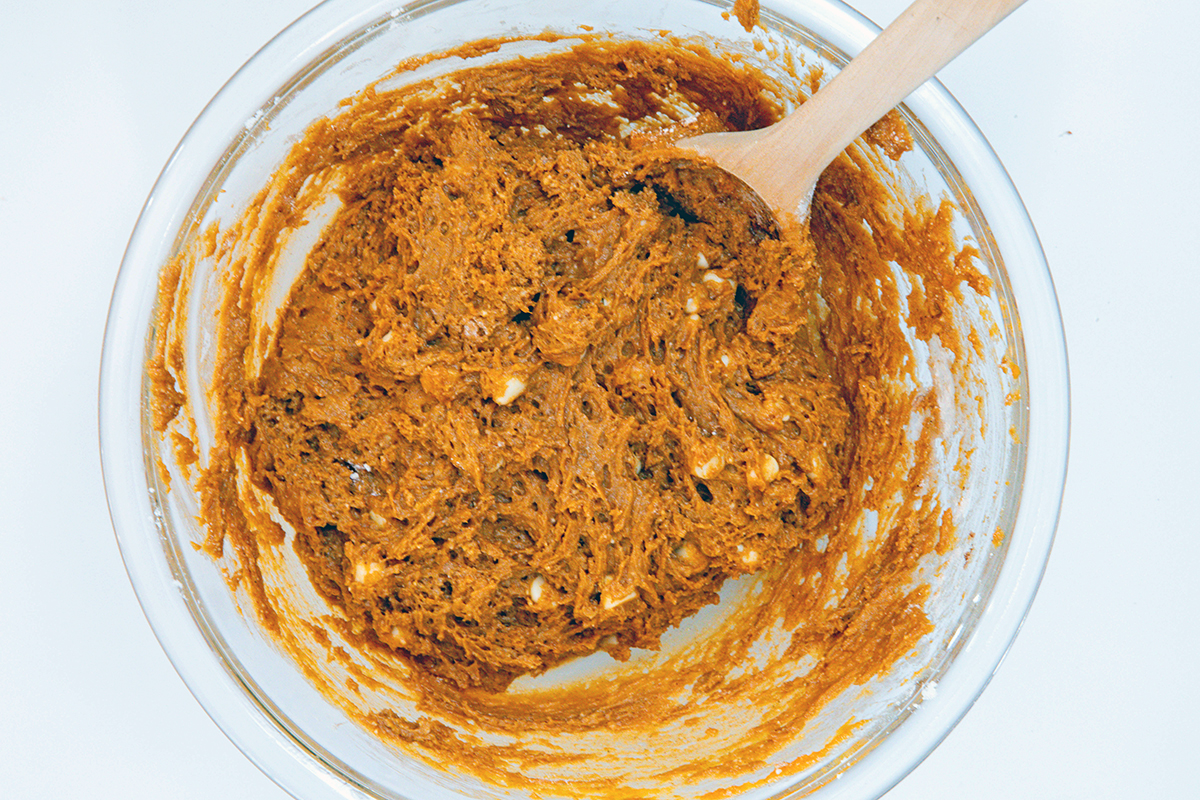 Landscape view of pumpkin cookie cake mix batter in mixing bowl with wooden spoon.