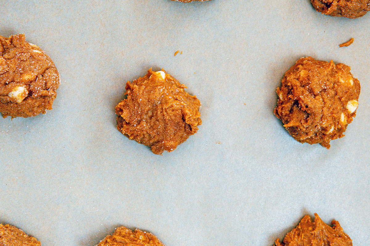 Landscape view of Pumpkin cookie dough balls on a parchment paper-lined baking sheet.