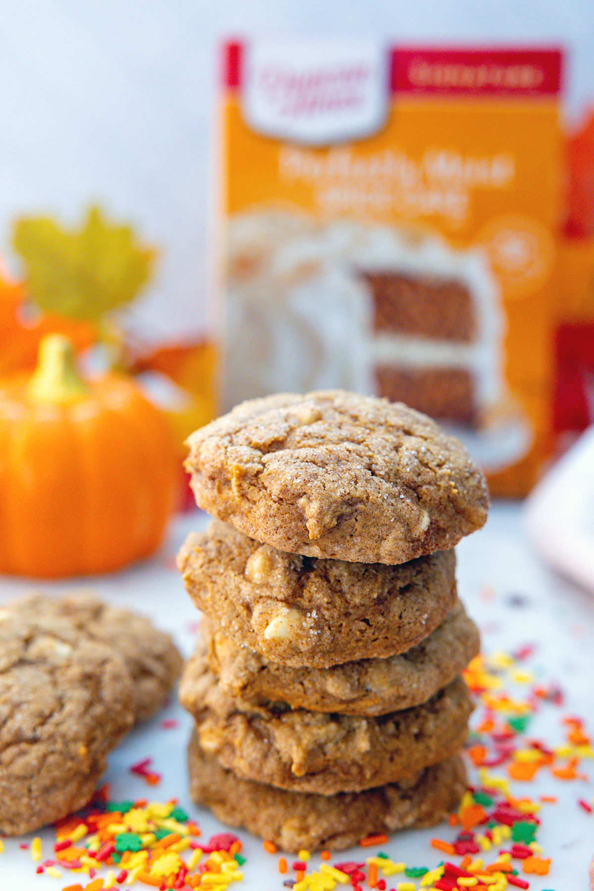 Head-on view of a stack of pumpkin white chocolate chip cookies with box of cake mix in background.