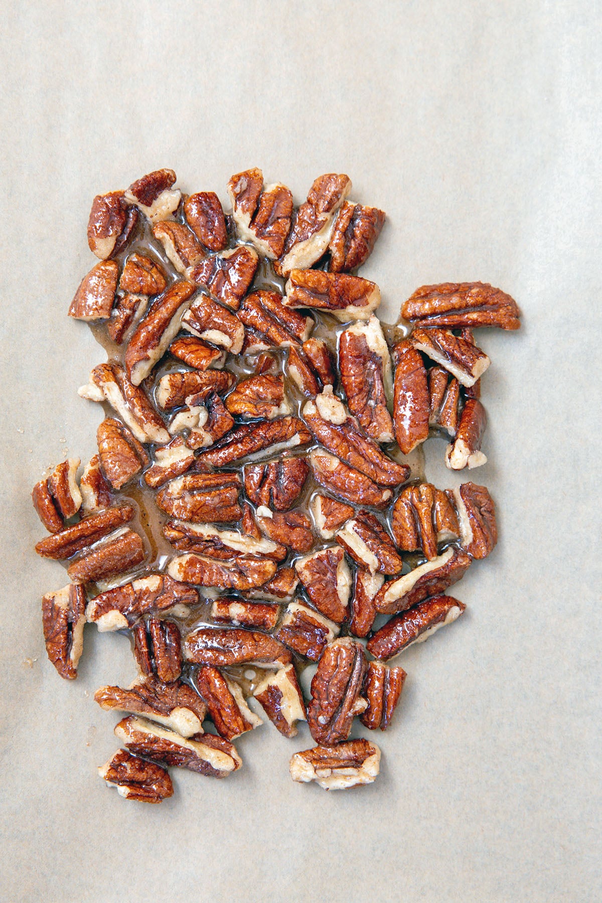 Pecans coated in syrup spread on parchment paper.