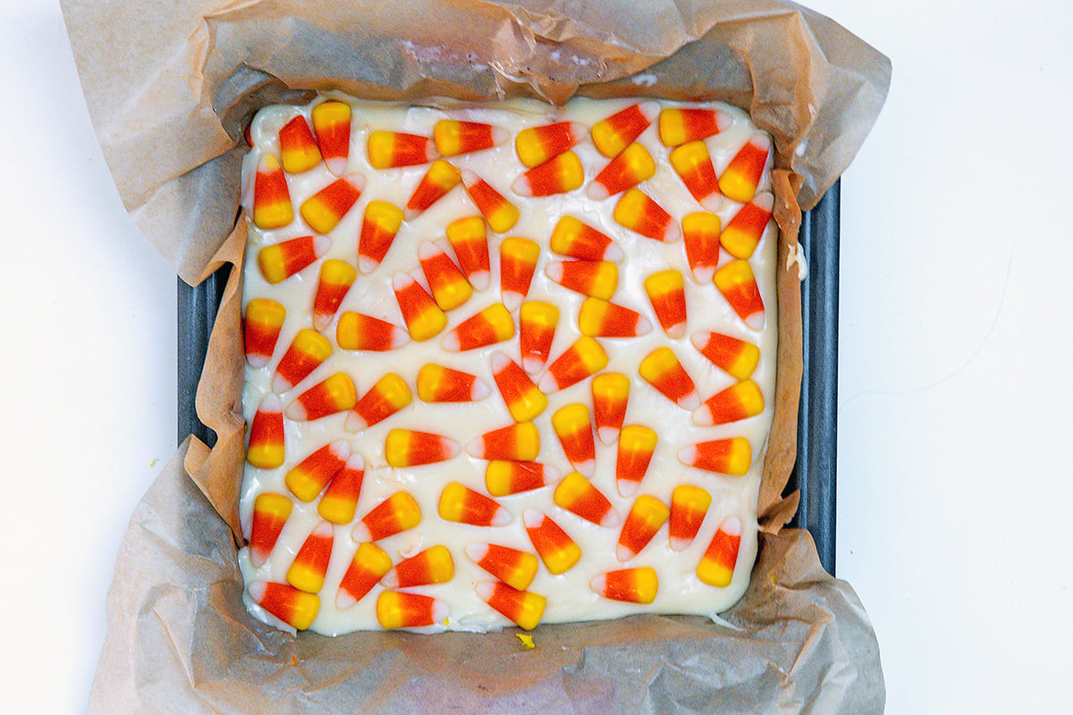 Landscape overhead view of white fudge topped with candy corn in square pan.