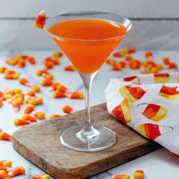 Closeup view of a candy corn martini with lots of candies around.