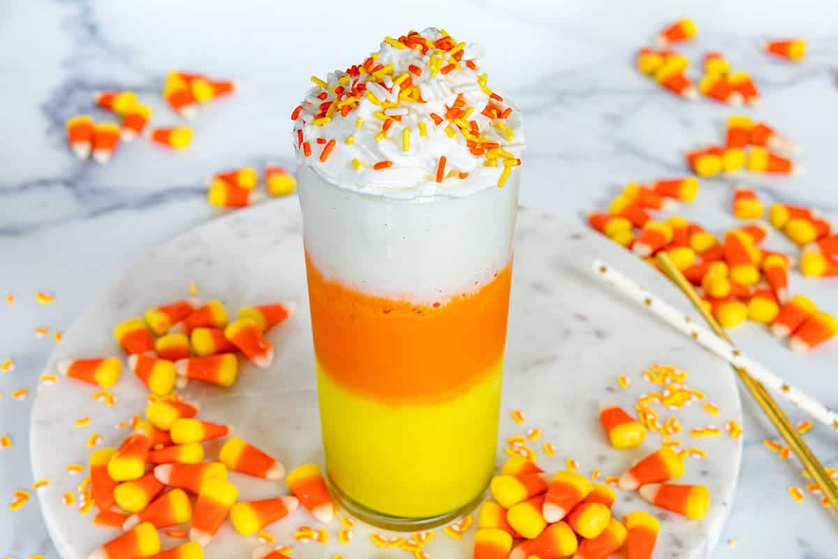 Landscape overhead view of a candy corn milkshake with whipped cream and orange and yellow sprinkles and candy corn all around.