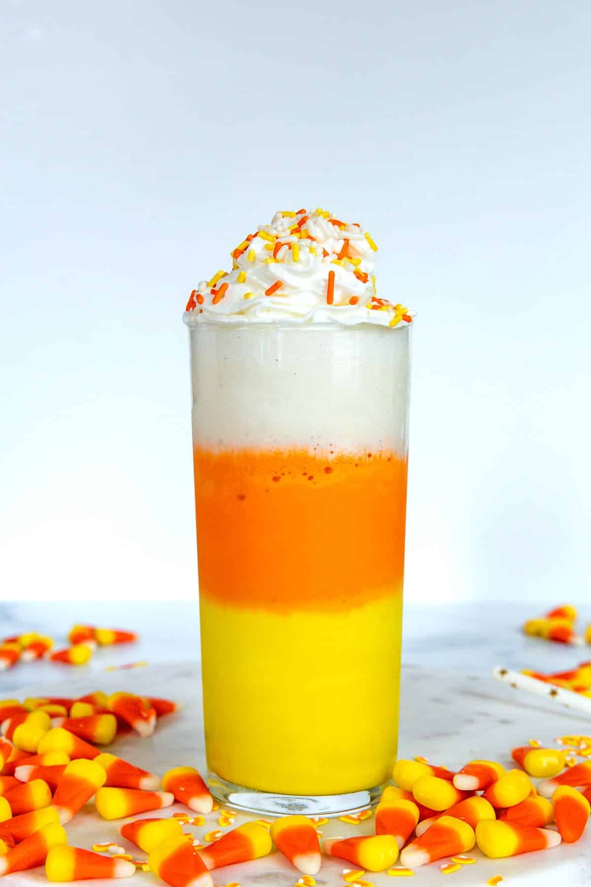 Head-on view of a yellow, orange, and white layered milkshake topped with whipped cream with candy corn all around.