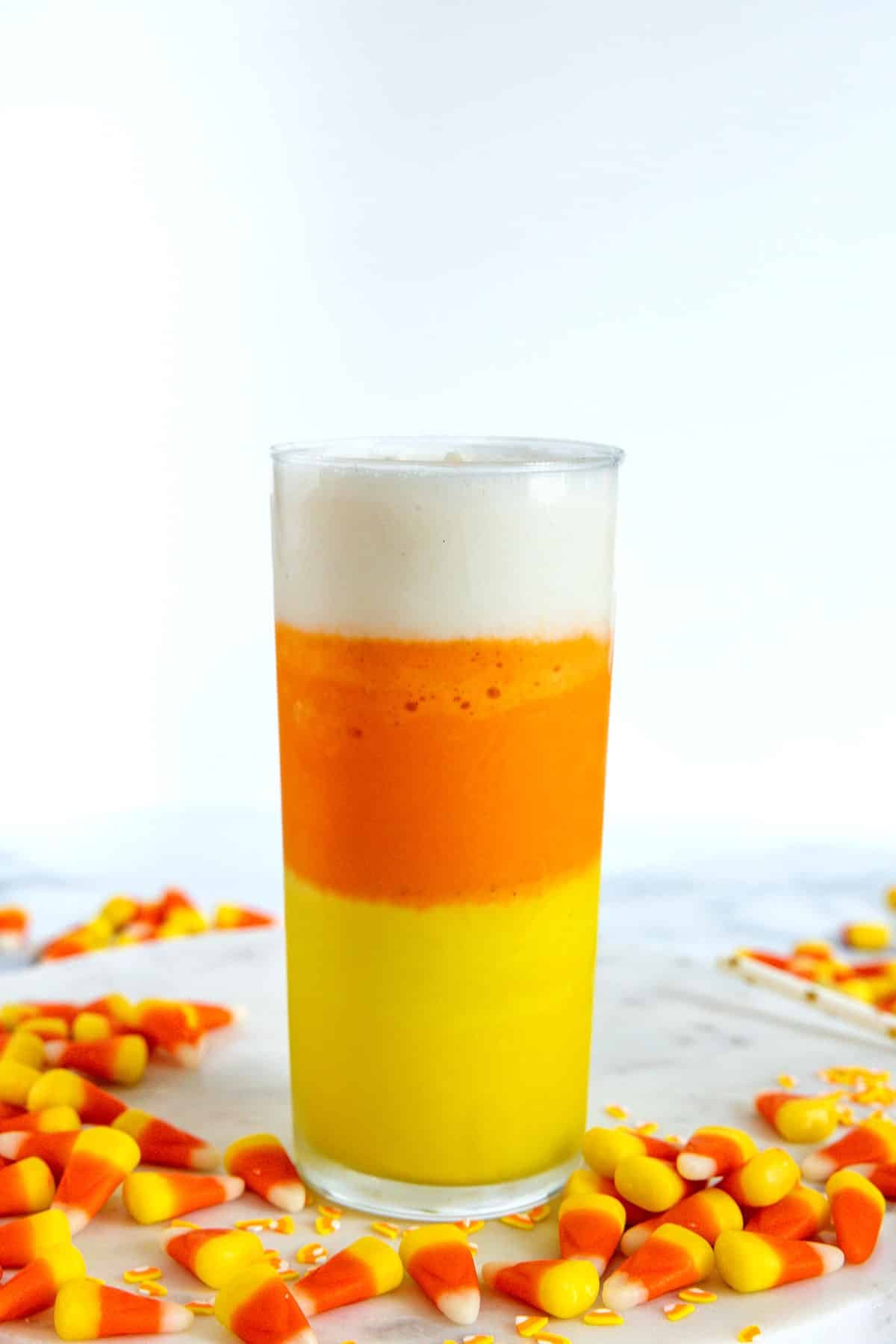 Yellow, orange, and white layered candy corn milkshake with candies all around.