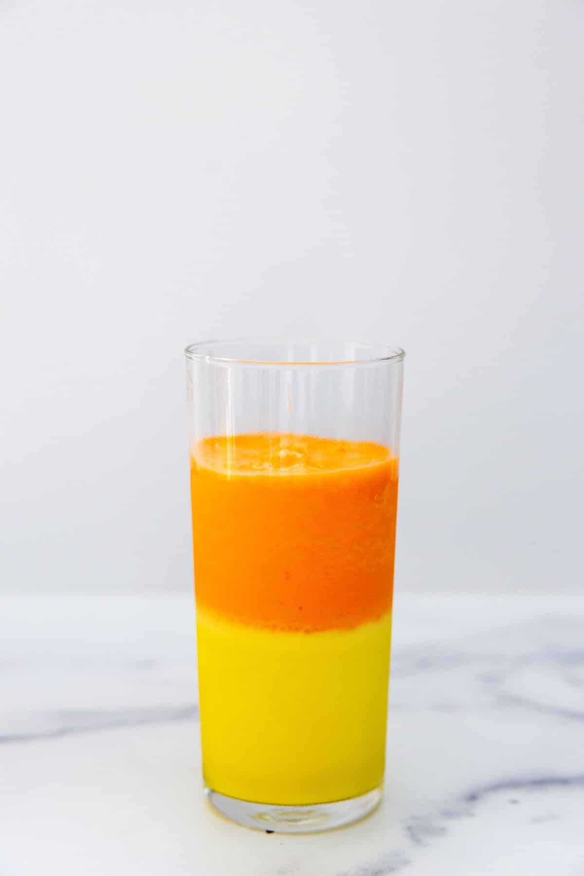 Glass filled with a layer of yellow milkshake and a layer of orange milkshake with some room at the top.