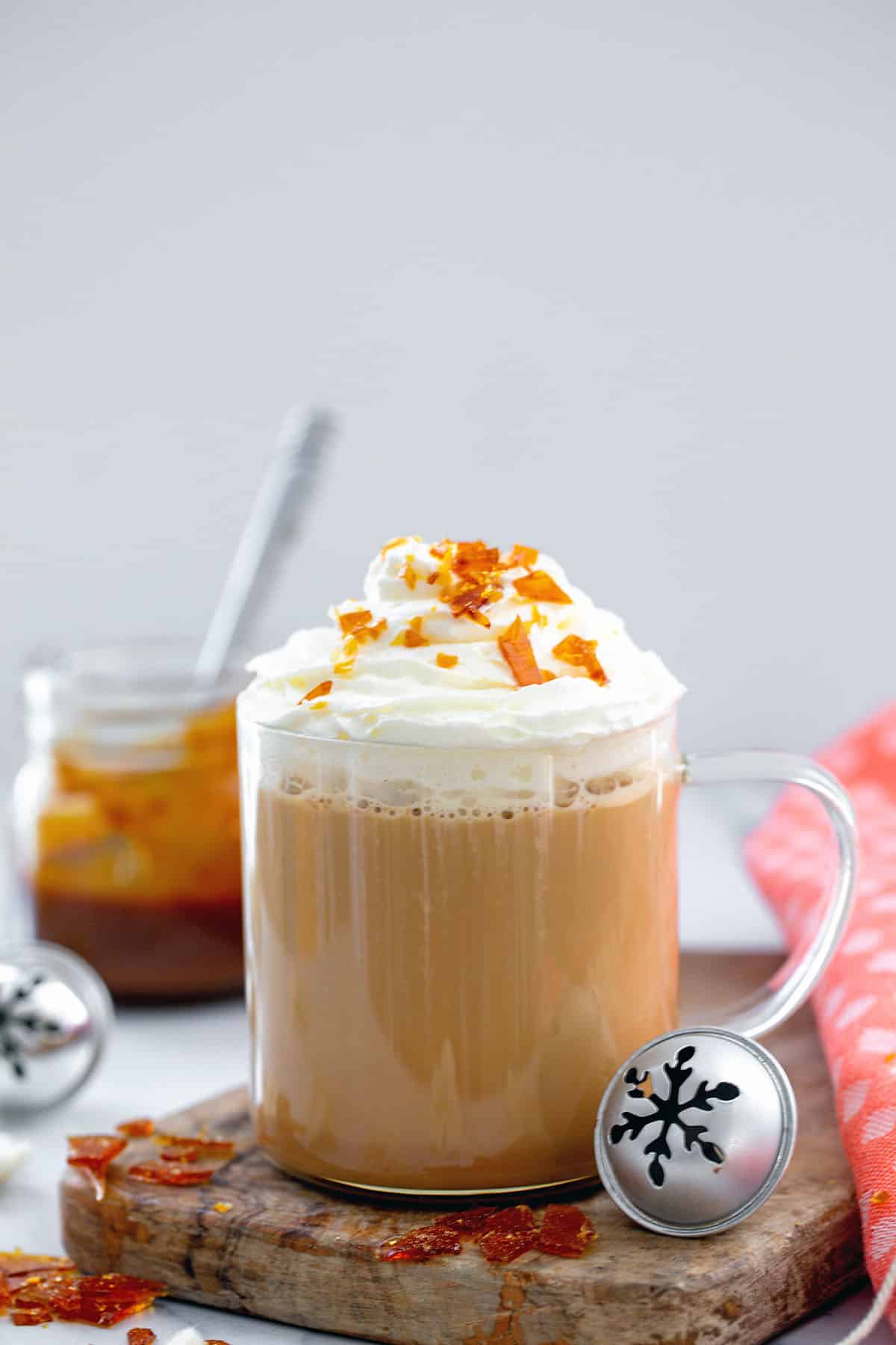 Head-on view of a Caramel Brulée Latte in a clear glass mug with caramel pieces and silver bell.