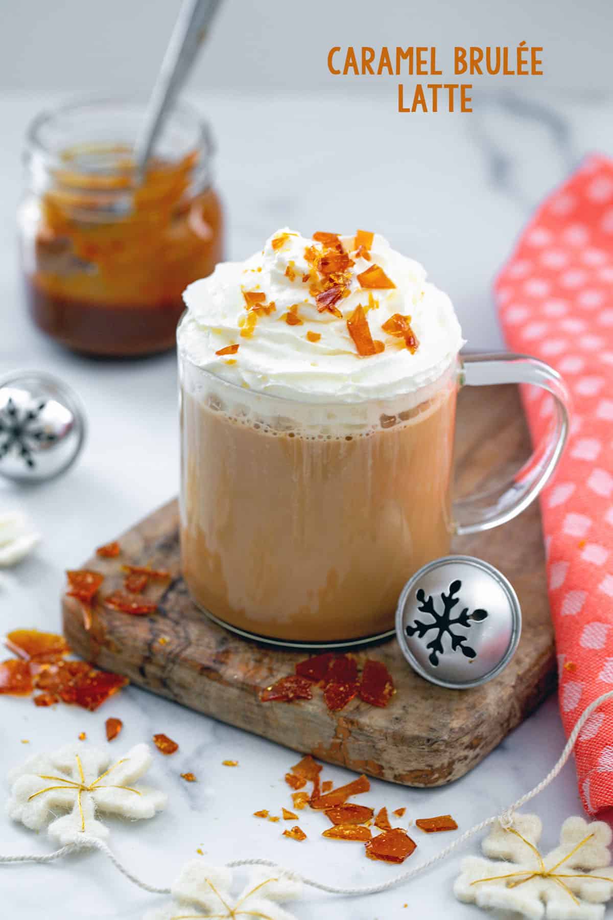 Mug with caramel brulée latte topped with whipped cream and brulée pieces with jar of caramel in background and recipe title at top.