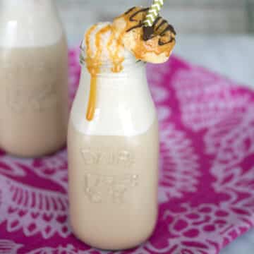 Closeup view of caramel coffee in a clear milk bottle with mini donut garnish and caramel drizzle.
