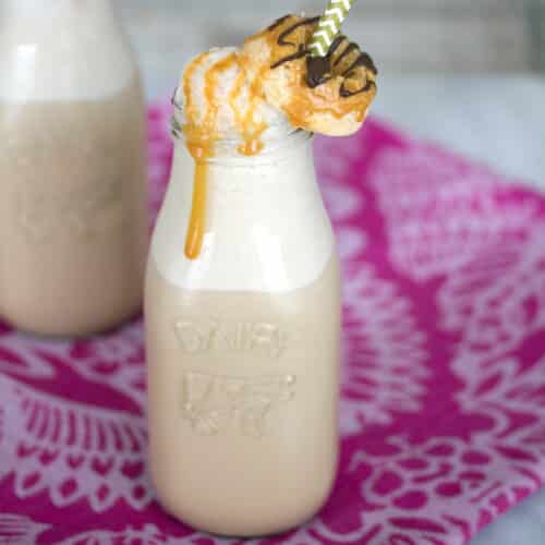 Closeup view of caramel coffee in a clear milk bottle with mini donut garnish and caramel drizzle.