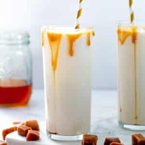 Head-on closeup view of glass of caramel milk with caramel drizzling down the sides.