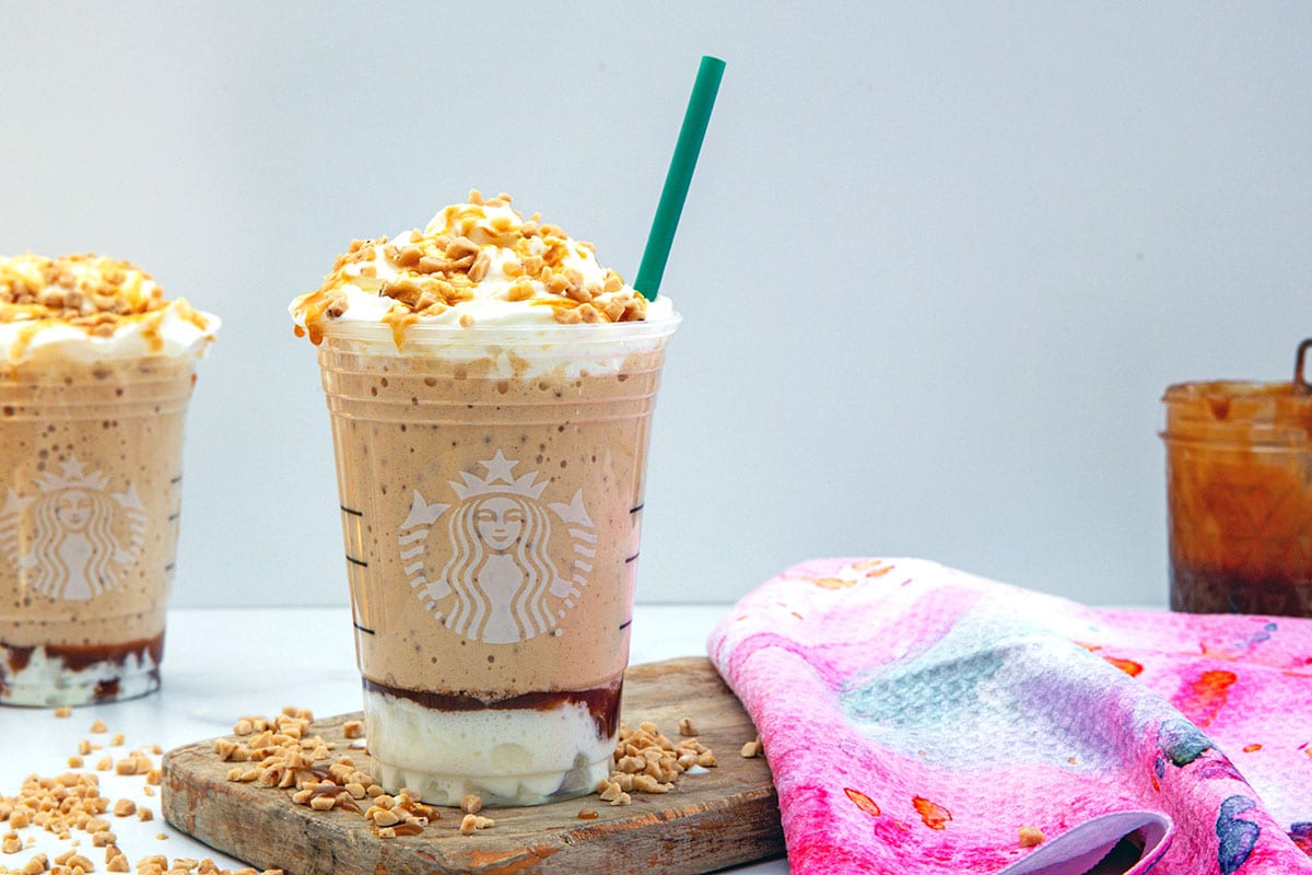 Landscape head-on view of a Caramel Ribbon Crunch Frappuccino with second drink in background.