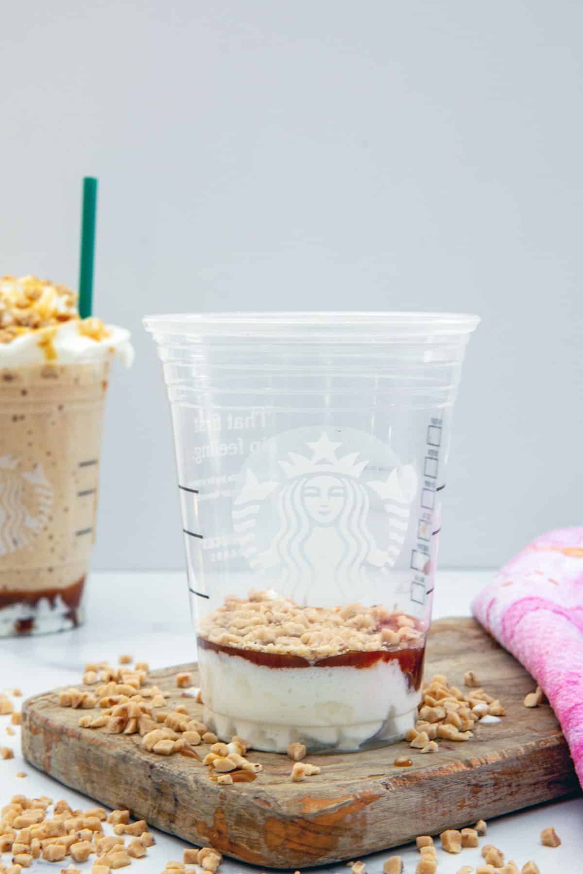 Starbucks cup with whipped cream, dark caramel sauce, and caramel crunch pieces.