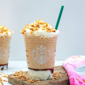 Closeup head-on view of a caramel ribbon crunch frappuccino with green straw.