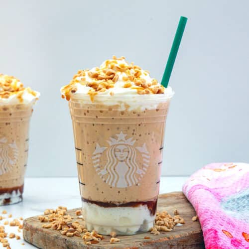 Closeup head-on view of a caramel ribbon crunch frappuccino with green straw.