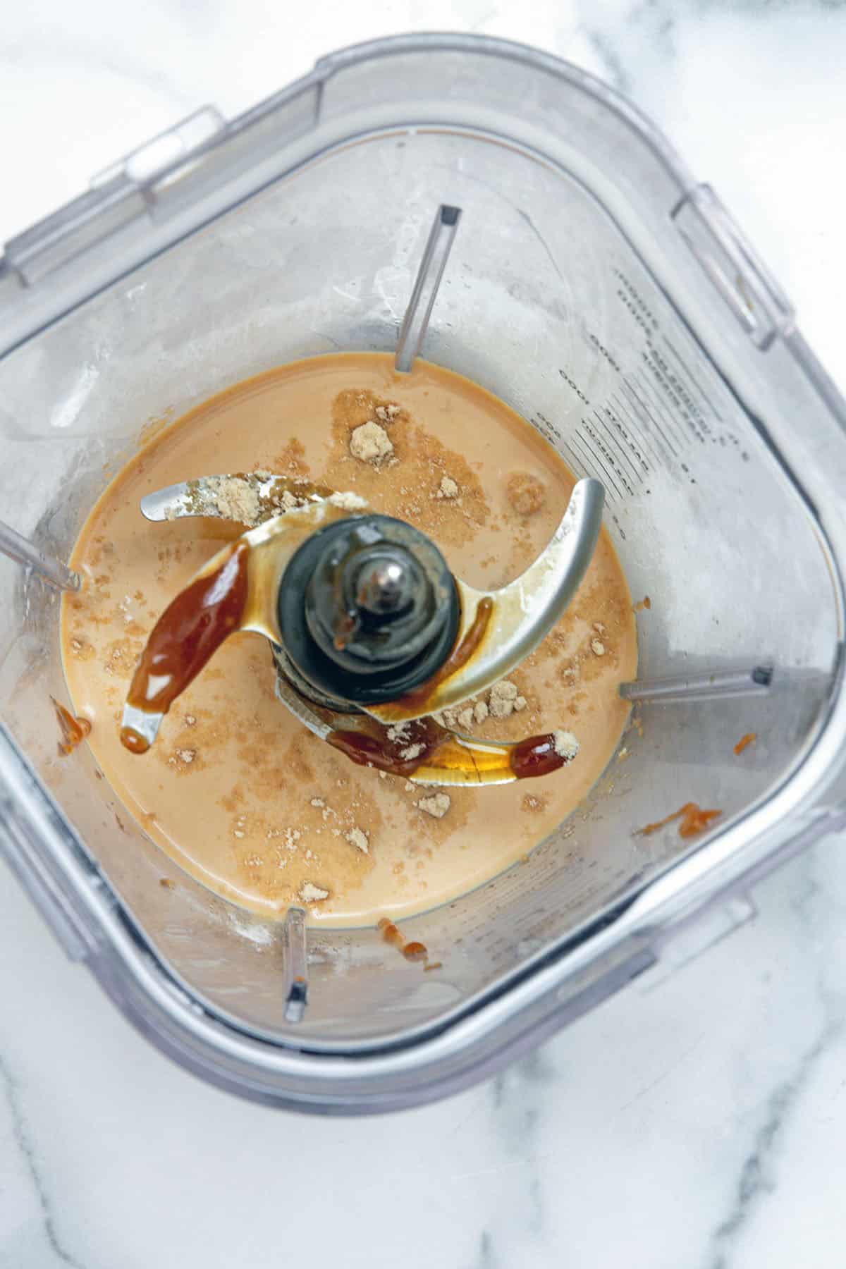 Overhead view of a blender with coffee, caramel, syrup, and milk.