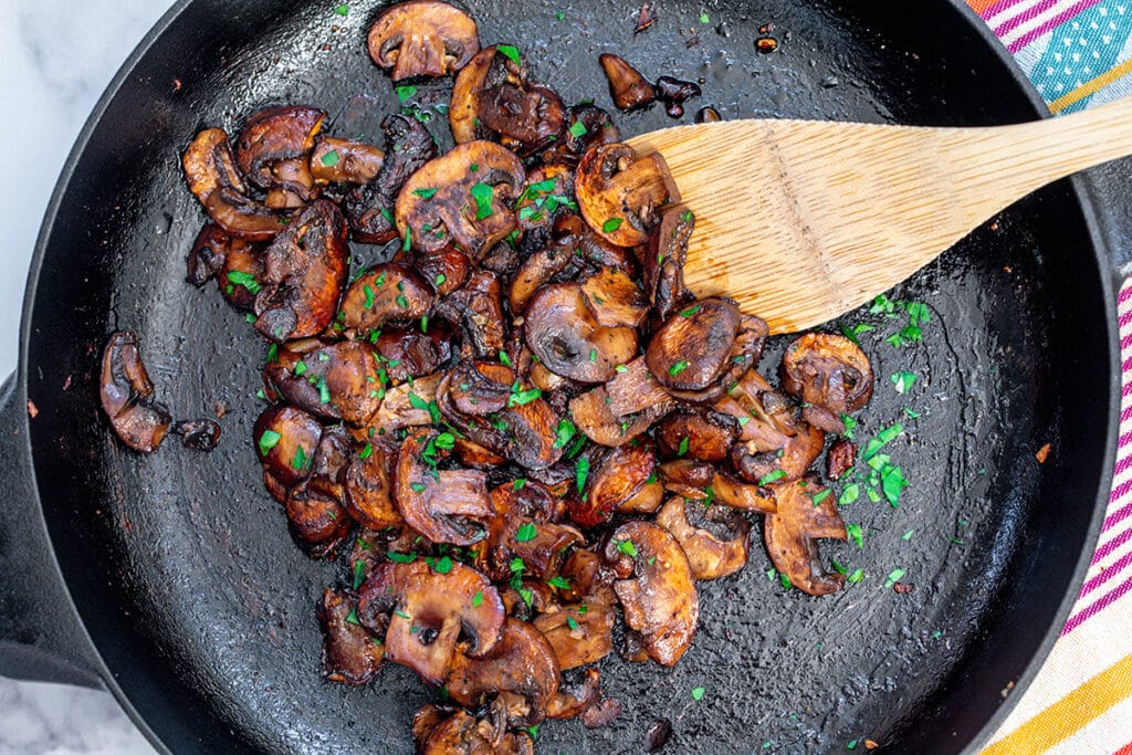 Landscape view of caramelized mushrooms with parsley in cast iron skillet.