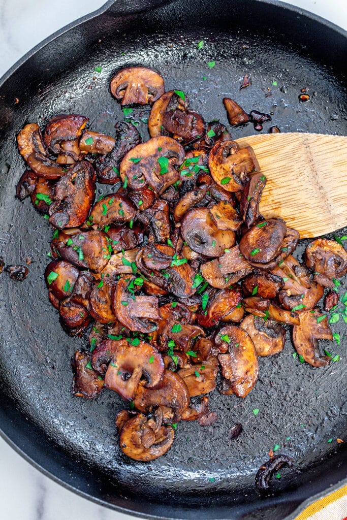 Caramelized mushrooms with parsley in cast iron skillet.