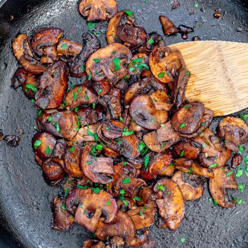 Closeup view of caramelized mushrooms in cast iron skillet with wooden spatula.