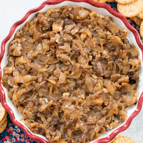Close-up view of a caramelized onion goat cheese dip in pie plate with crackers in background.