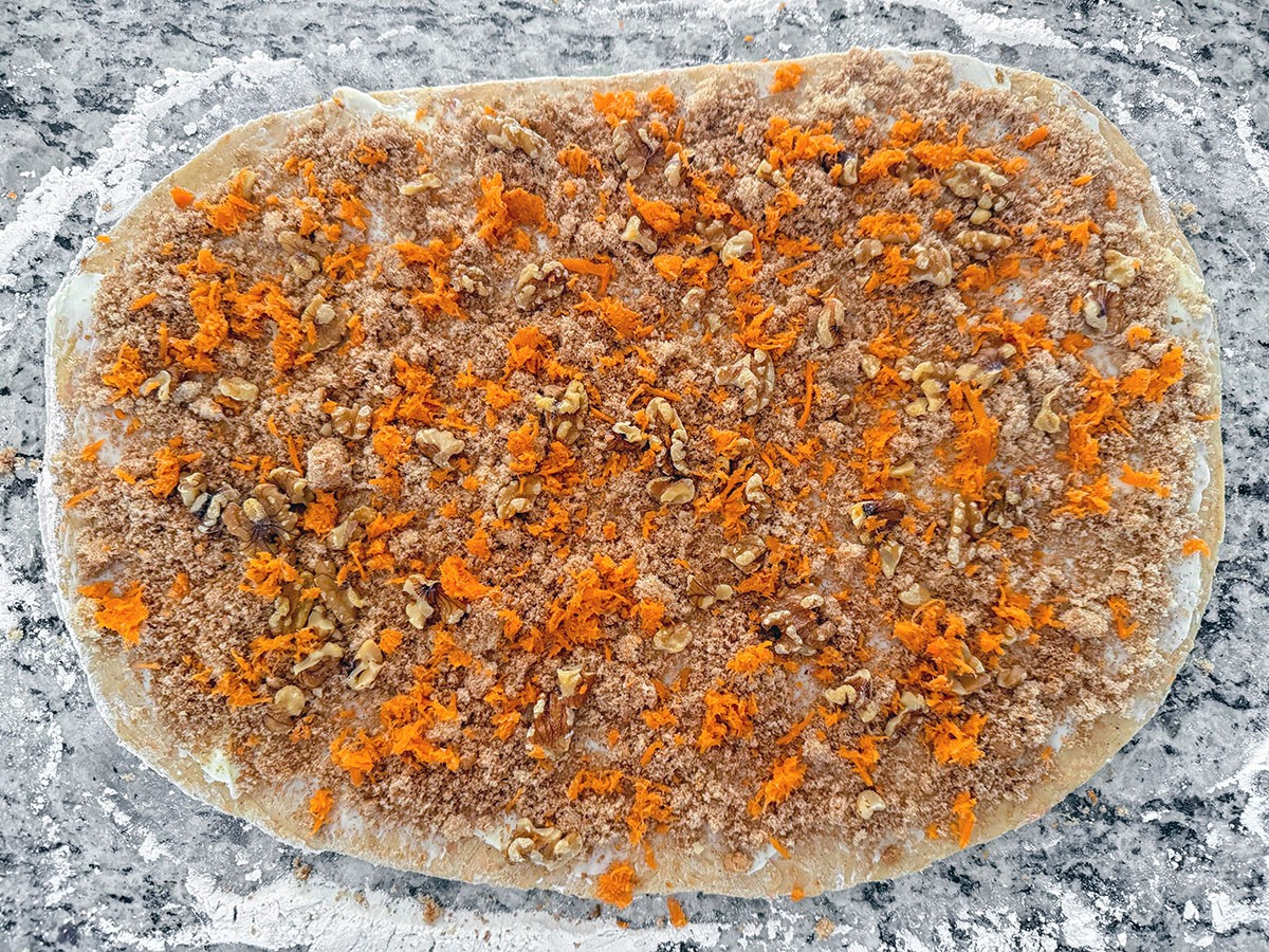 Cinnamon roll dough rolled out and topped with butter, brown sugar, grated carrots, and walnuts.
