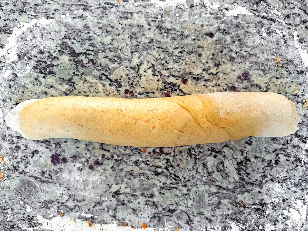 Cinnamon roll dough rolled up into tube on counter.
