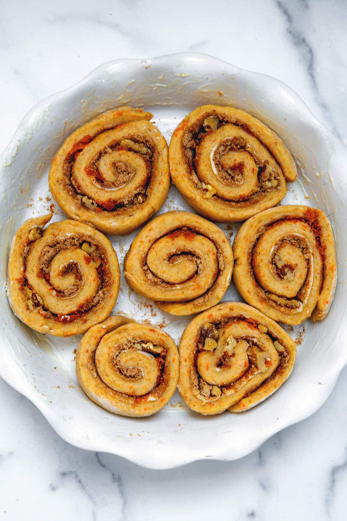 Unbaked carrot cake cinnamon rolls in a pie dish after second rise.